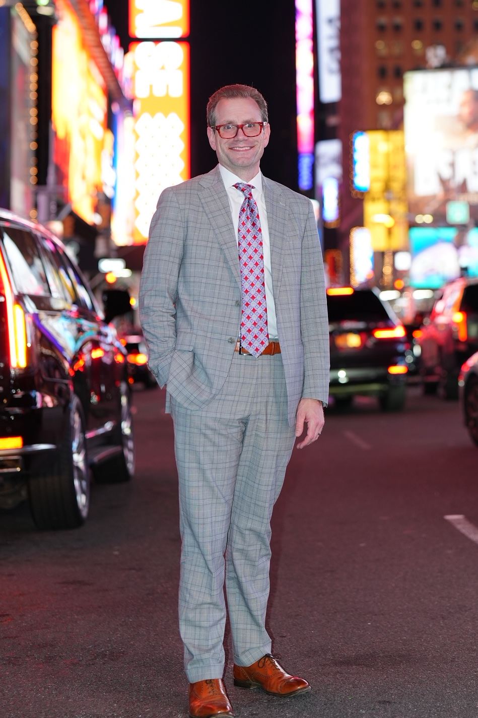 Austin Parker in a gray plaid suit standing in Times Square at night