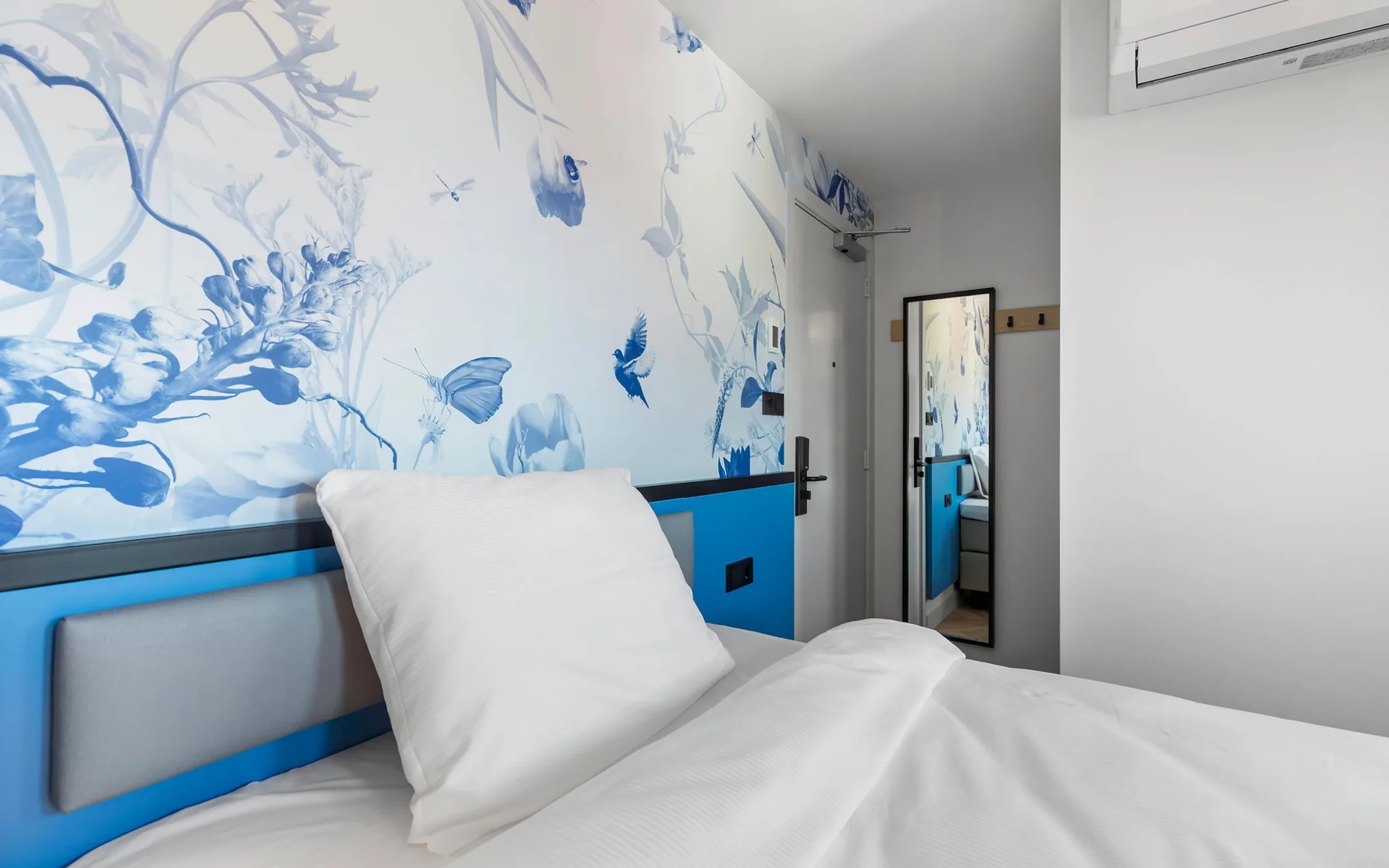 Hotel room with Delft blue wallpaper above a blue bedboard