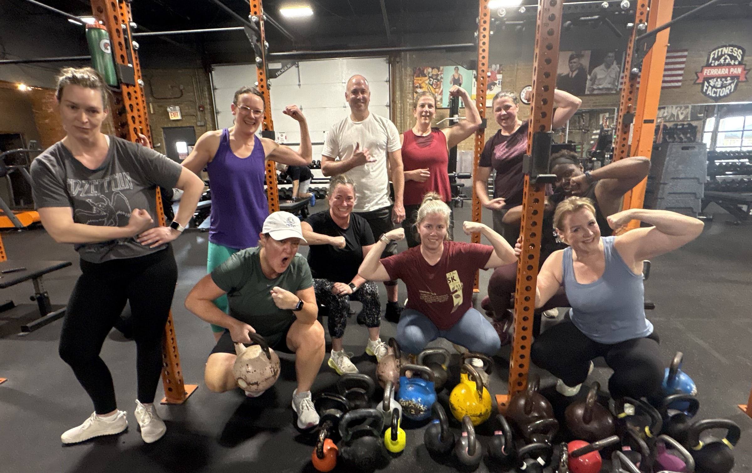 Group of ten Three Bears Fitness members flexing and posing with a pile of kettlebells in the gym
