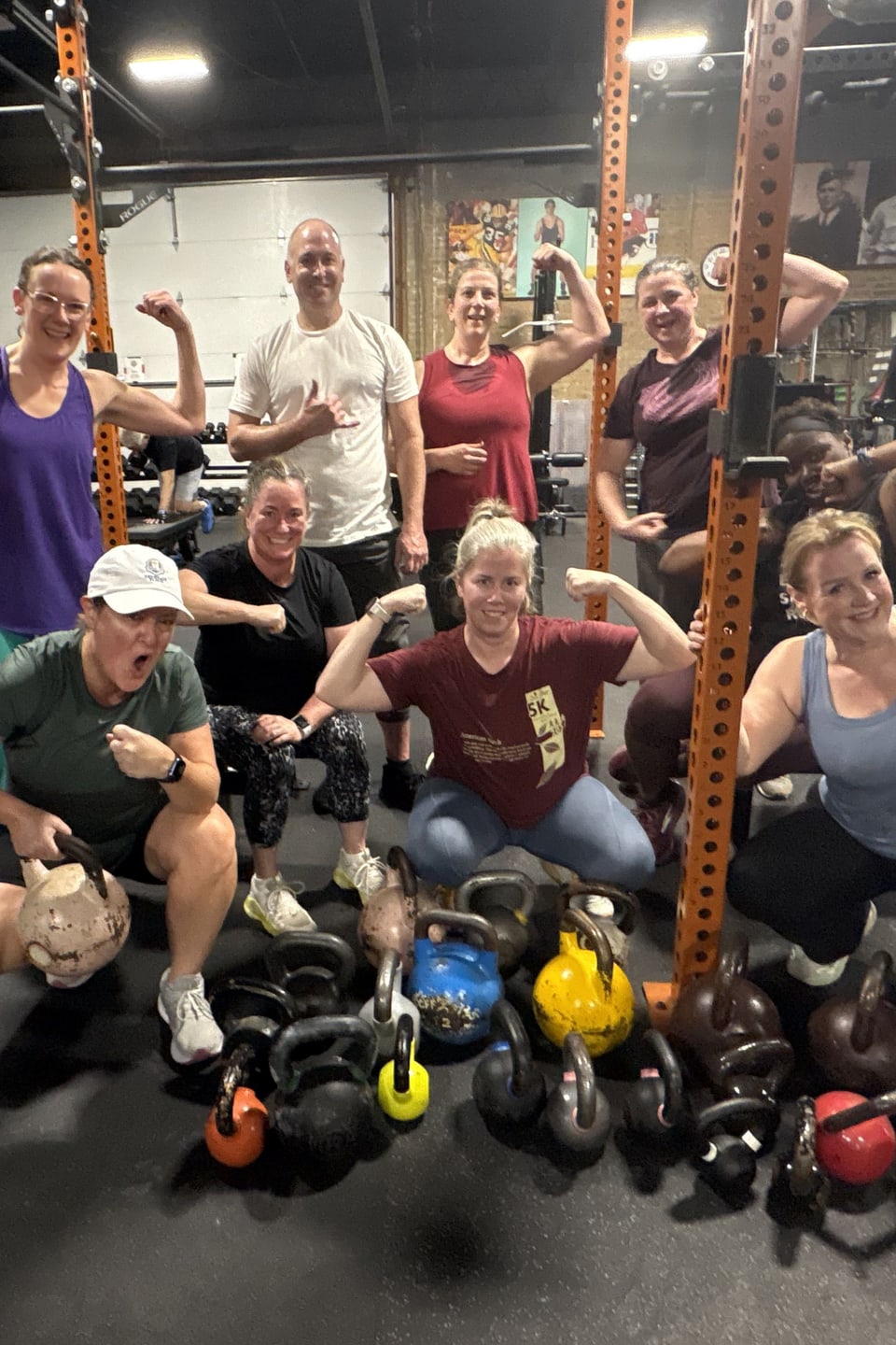Group of ten Three Bears Fitness members flexing and posing with a pile of kettlebells in the gym