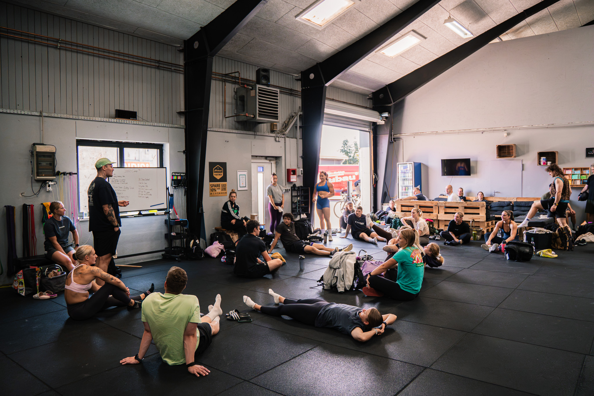 Coach erklärt das Workout am Whiteboard, die Gruppe sitzt auf dem Hallenboden