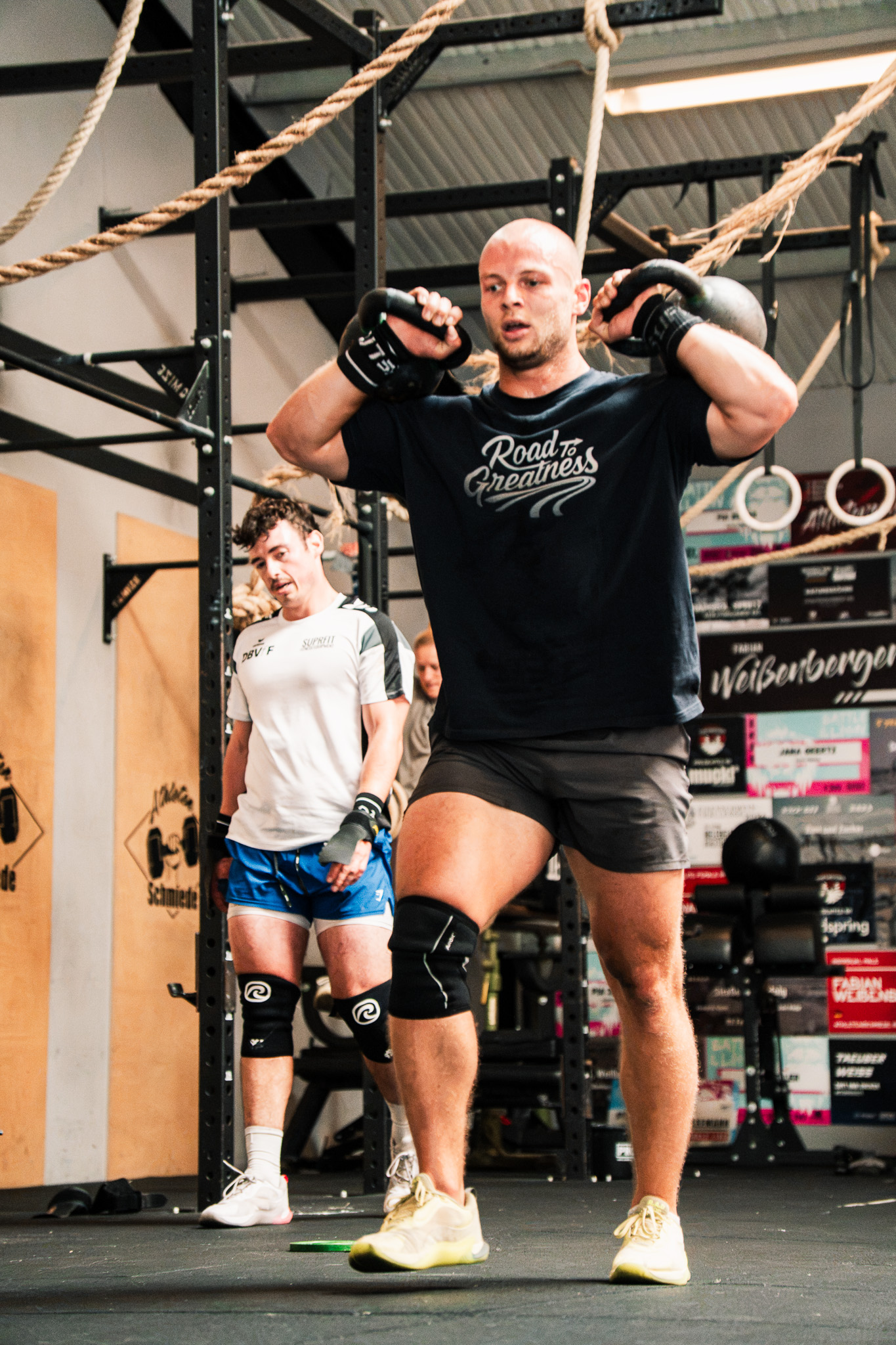 Athlet im Road to Greatness Shirt trägt zwei Kettlebells auf den Schultern