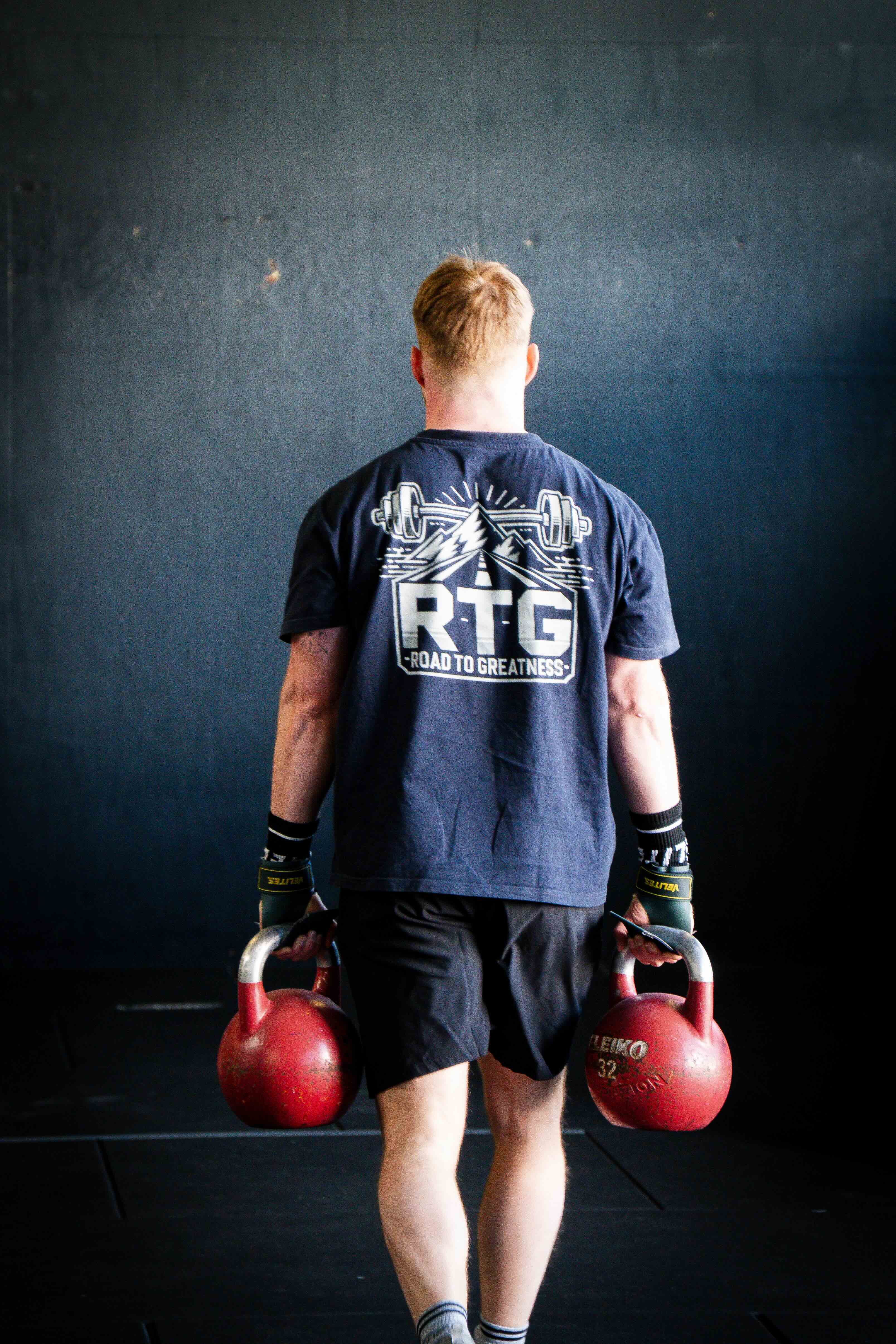 Athlet im RTG Shirt trägt zwei Kettlebells, von hinten fotografiert