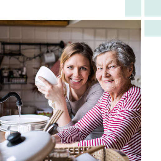 A woman and an older woman collaborate in a bright kitchen, sharing a moment of joy while preparing a meal together.