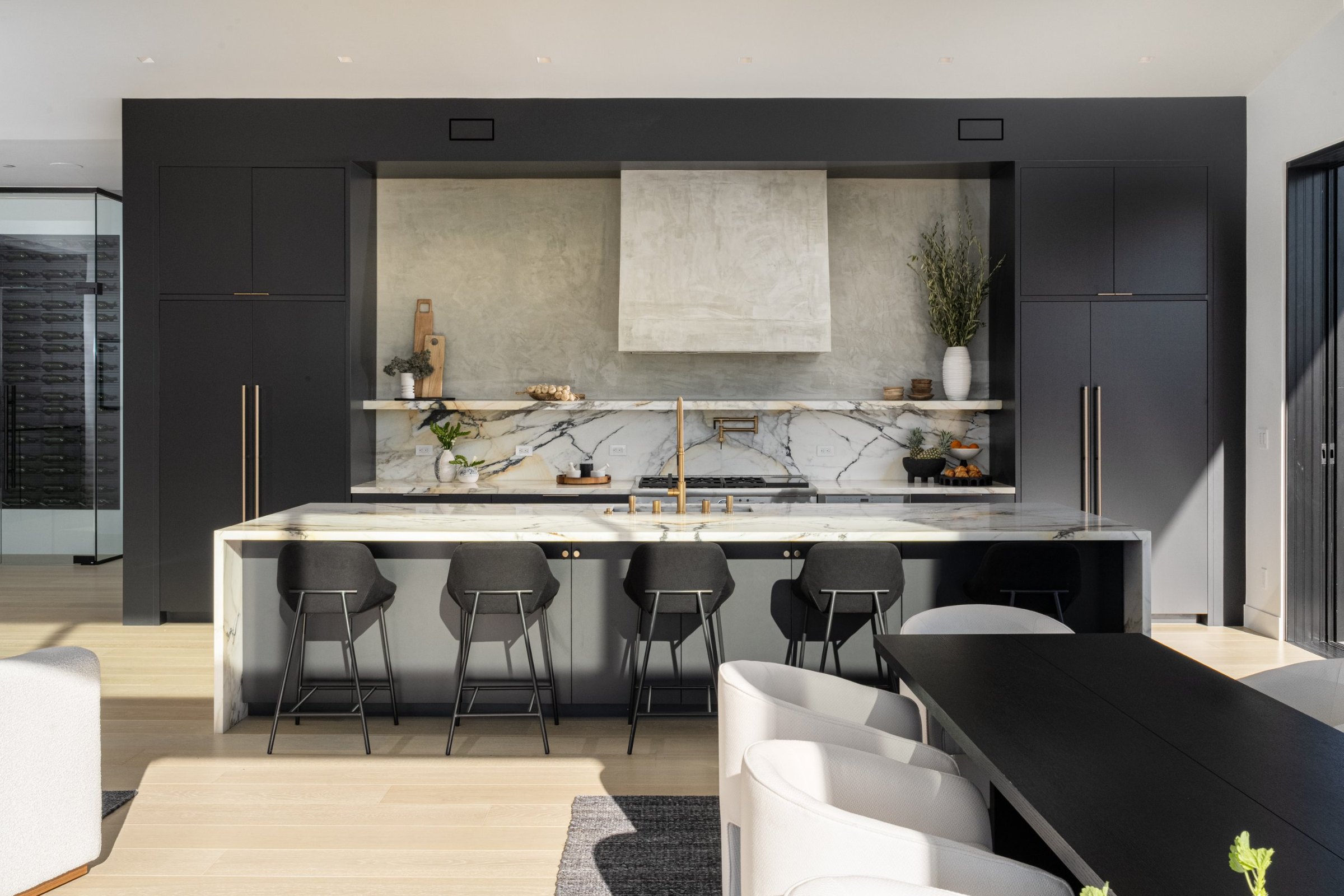 A black kitchen with a marble waterfall island and brass fixtures, San Francisco Bay Area. Real estate photography by Lumiful Media