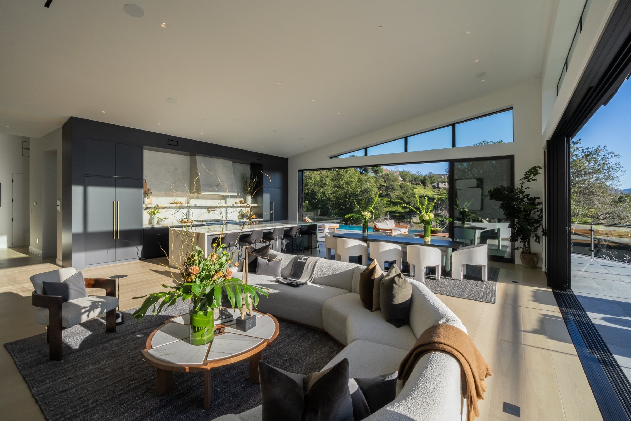 Afternoon sun across a great room with a curved sofa, open to the pool terrace, San Francisco Bay Area. Real estate photography by Lumiful Media