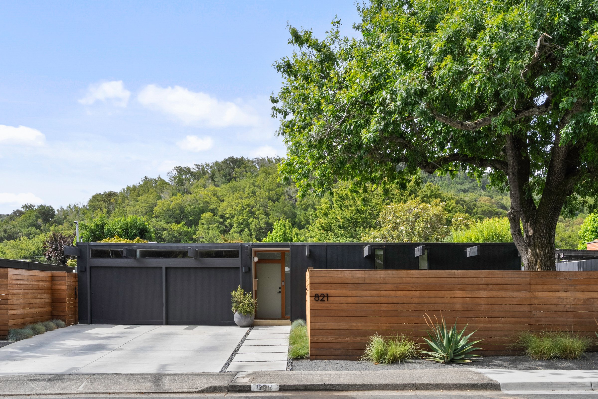 A dark modern facade and wood fence under an old oak, San Francisco Bay Area. Real estate photography by Lumiful Media