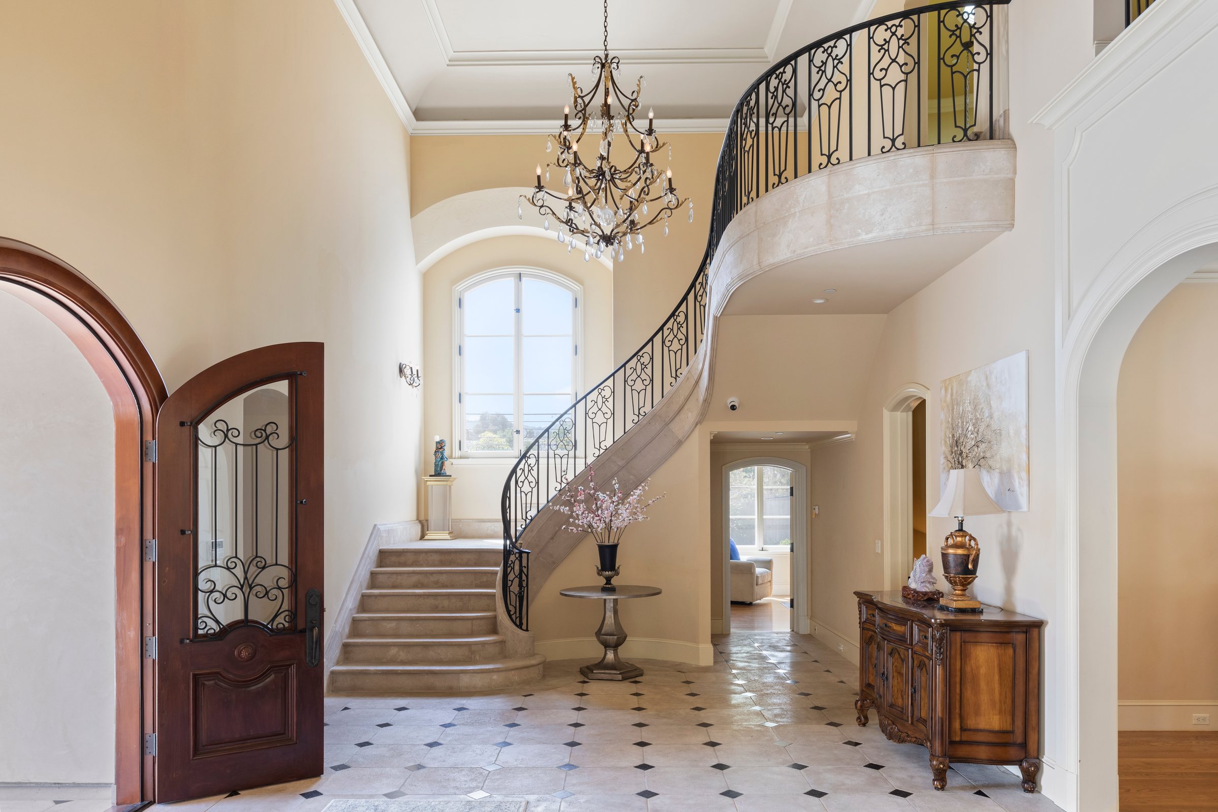 A grand entry with a curved iron stair and chandelier, San Francisco Bay Area. Real estate photography by Lumiful Media