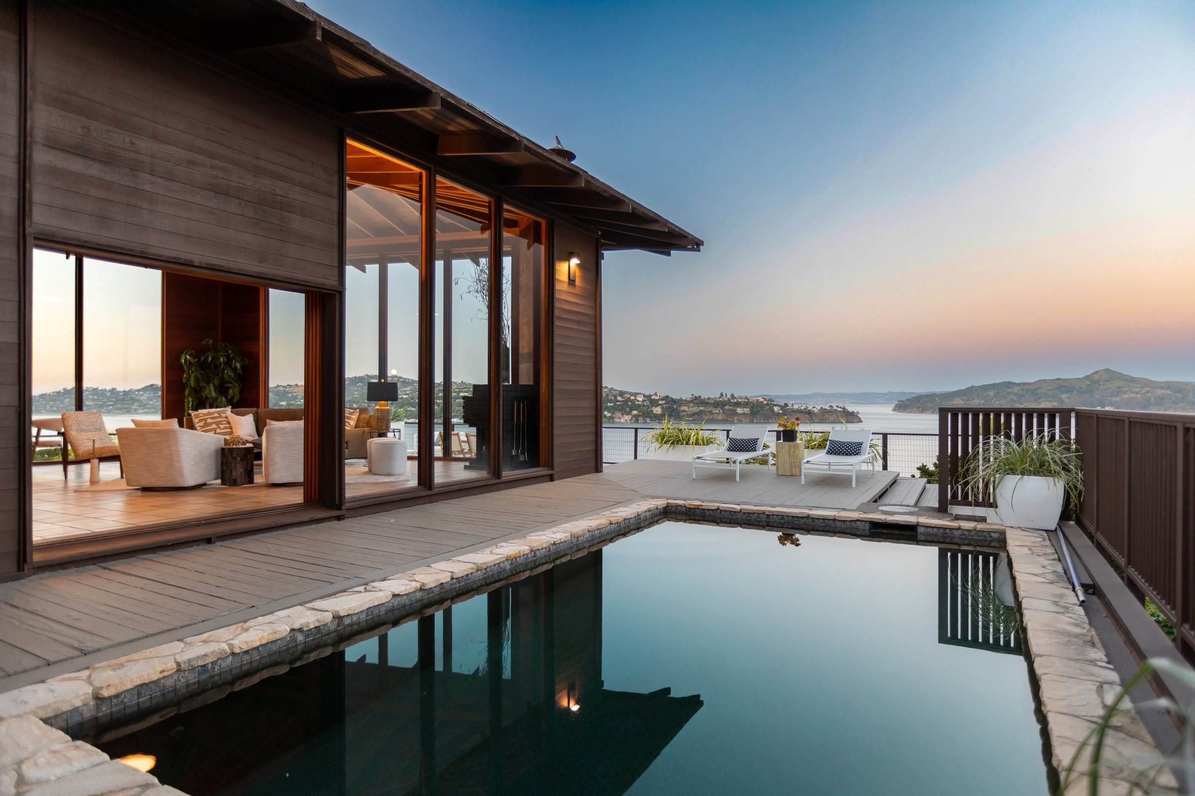 A lit living room and lap pool above the bay at dusk, San Francisco Bay Area. Twilight real estate photography by Lumiful Media