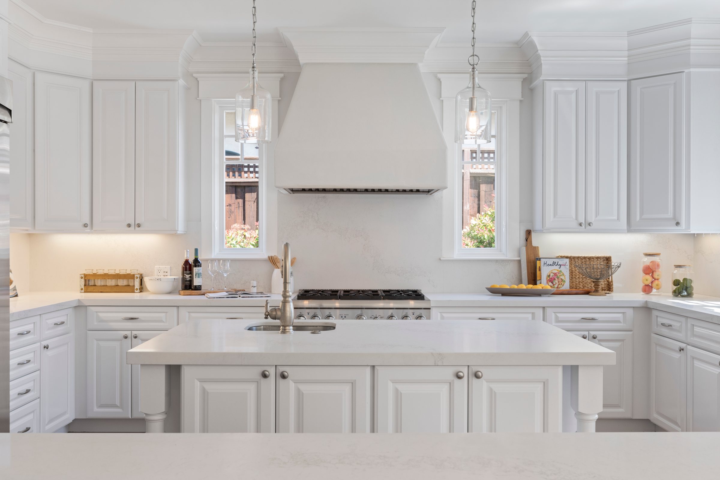 A white kitchen with a large island and glass pendants, San Francisco Bay Area. Real estate photography by Lumiful Media