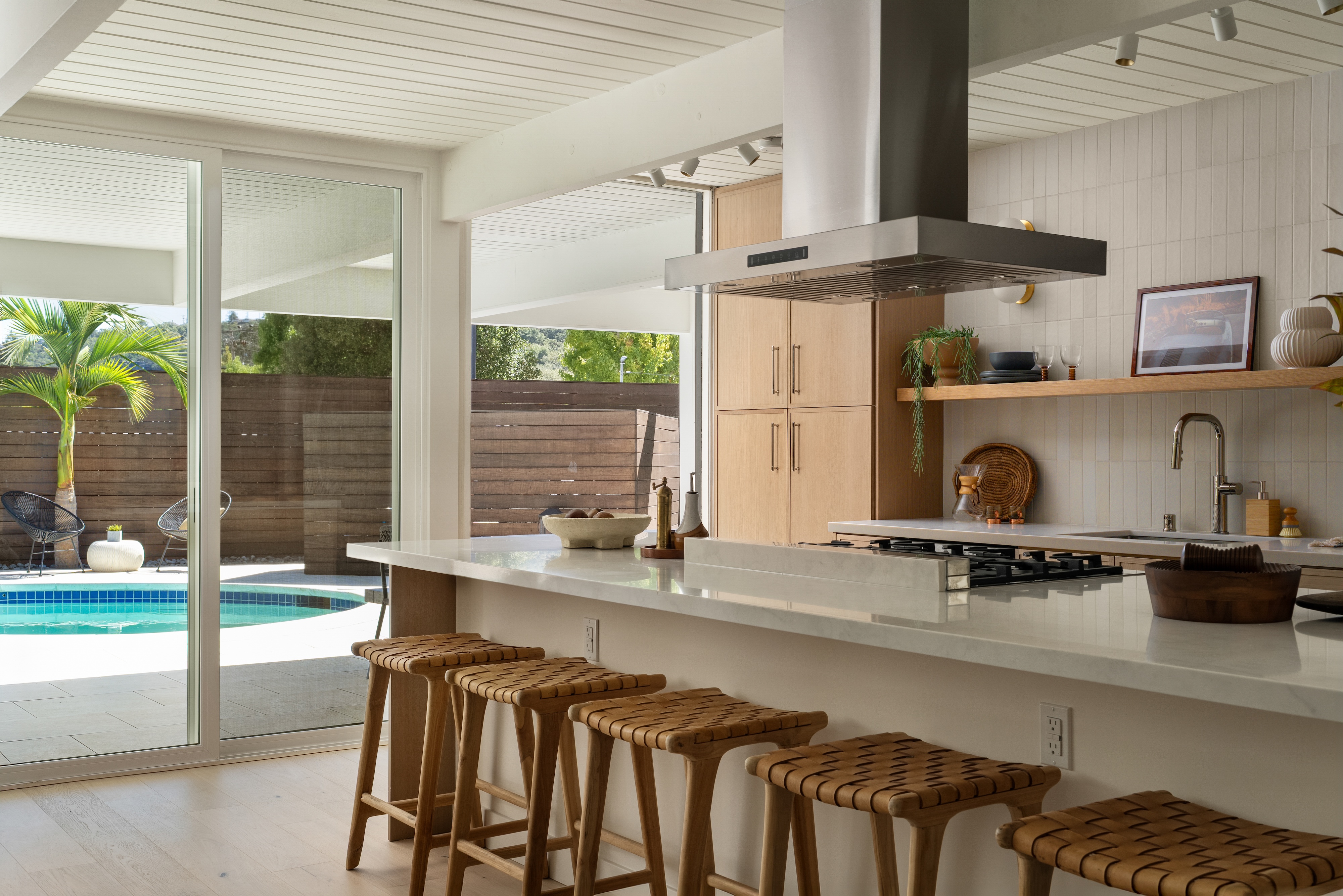A midcentury kitchen with woven stools, open to the pool, San Francisco Bay Area. Editorial interior photography by Lumiful Media