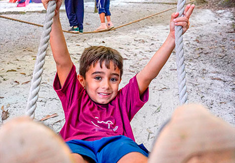 Criança sorri enquanto usa um balanço no parque de areia da escola