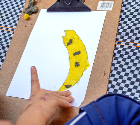 Criança aponta para pintura de uma banana feita em atividade de observação