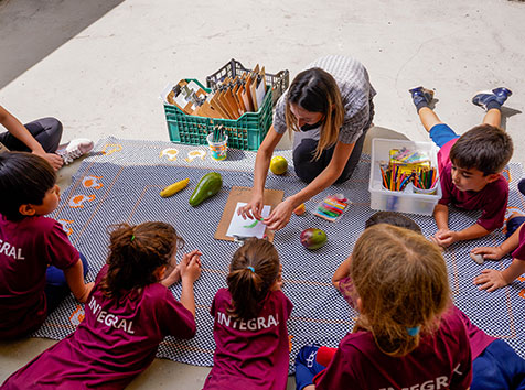 Educadora orienta crianças reunidas em atividade com frutas, desenhos e pintura