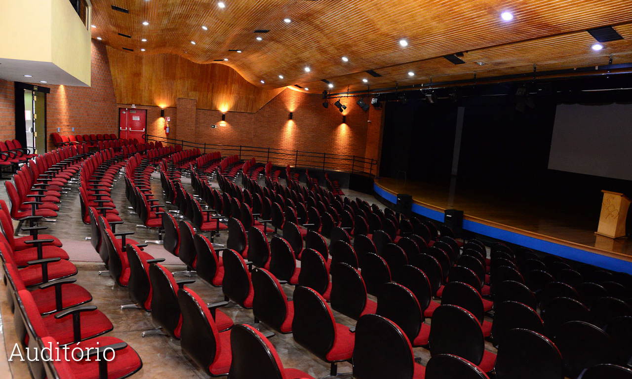 Auditório vazio com fileiras de poltronas vermelhas voltadas para o palco