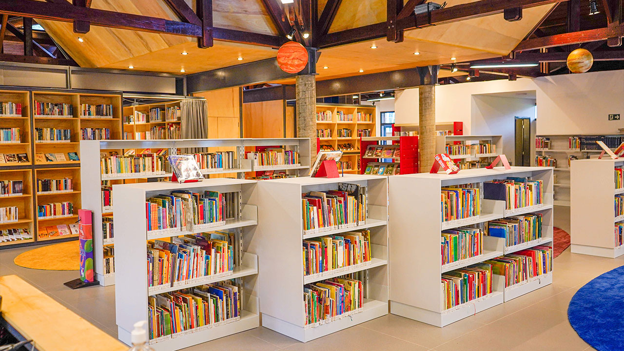 Biblioteca infantil com estantes baixas, livros coloridos e móbiles do sistema solar