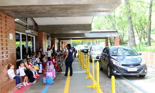 Área coberta de embarque e desembarque com estudantes, famílias e carros