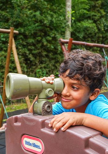 Menino olha por uma luneta de brinquedo no parque do Colégio