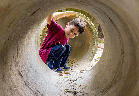 Menino espia de dentro de um tubo de concreto no parque