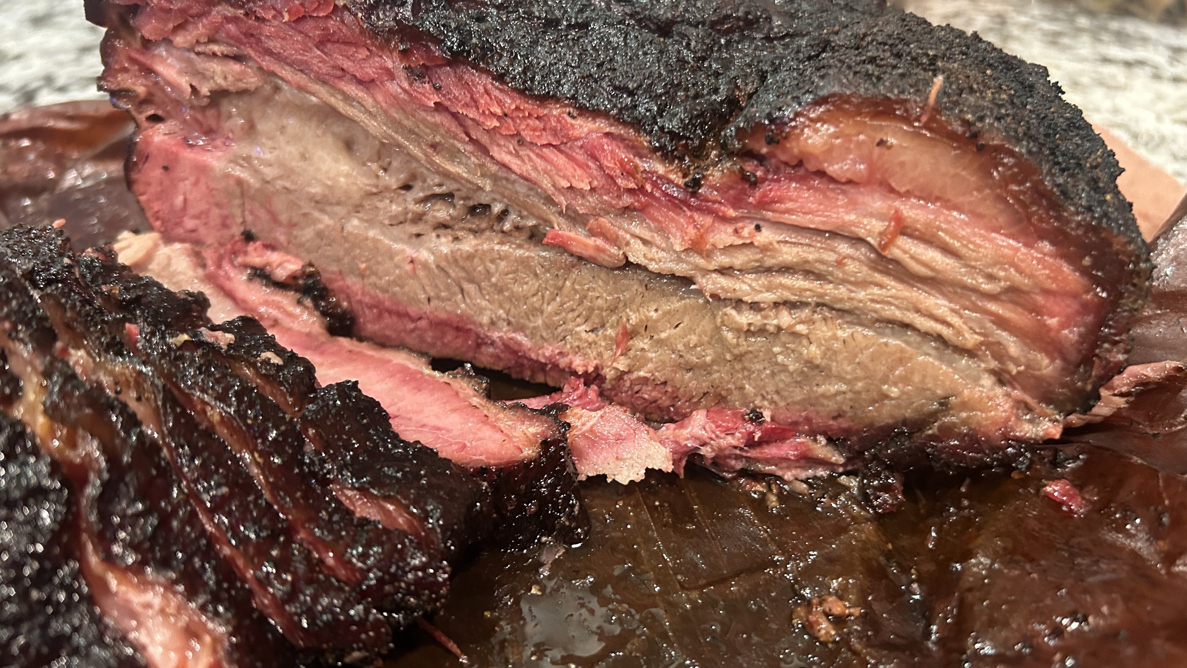Sliced smoked brisket with dark bark and pink smoke ring on butcher paper