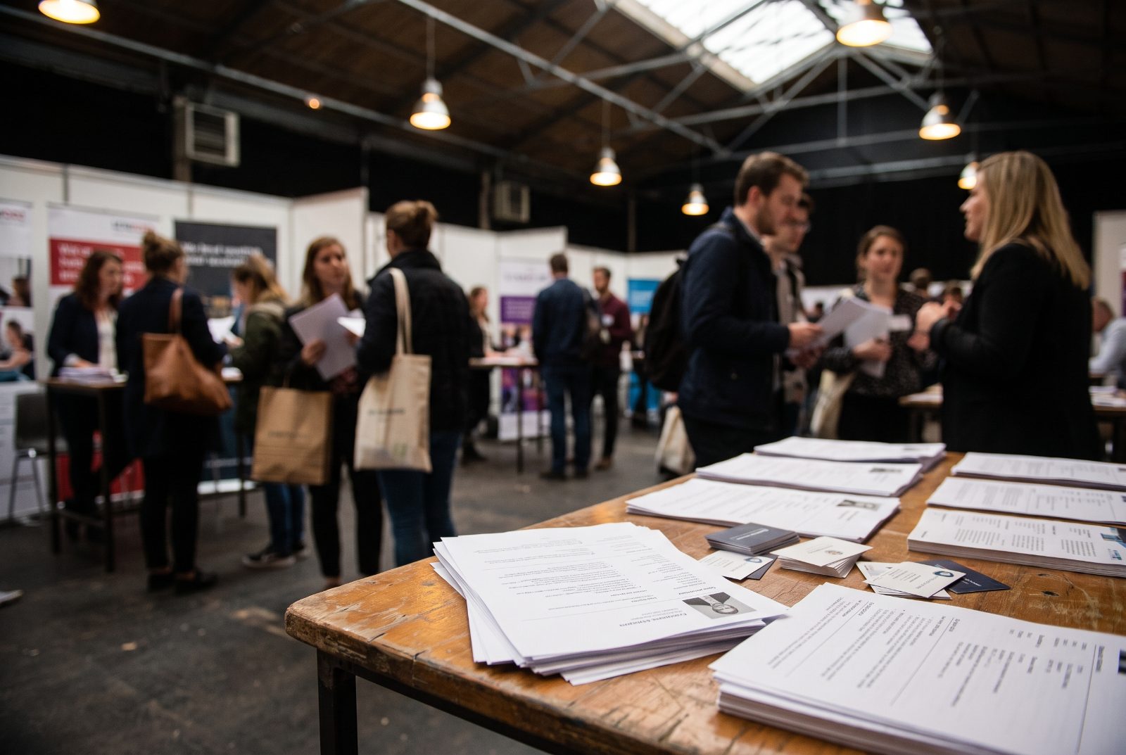 Une pile de CV papier sur une table de stand, dans un salon emploi.