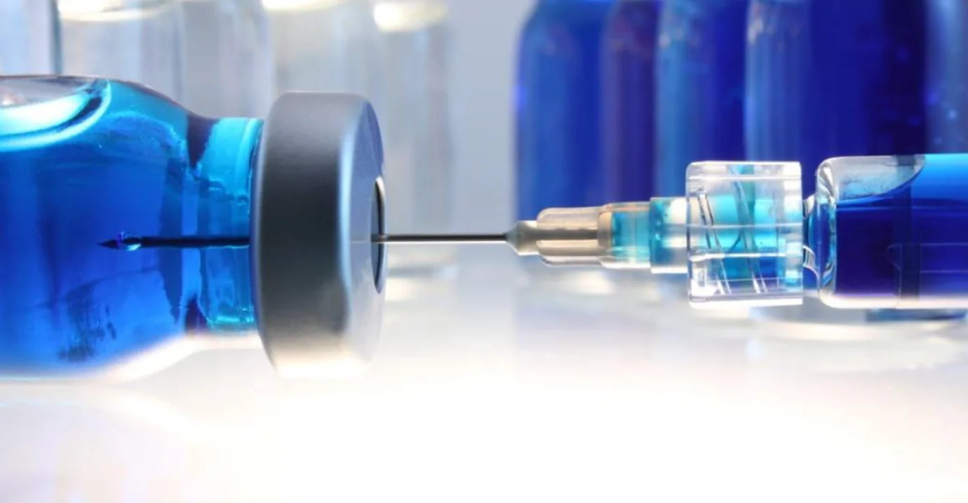 Syringe drawing blue liquid from a vial