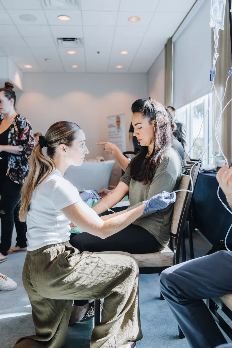A trainee kneels to place an IV in a volunteer's arm during hands-on practice at a live training
