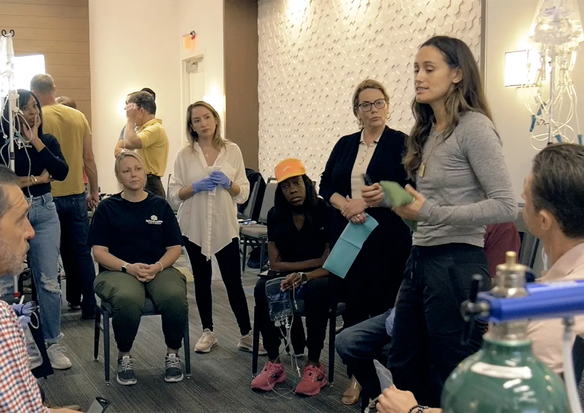 A small group of clinicians in gloves gathers around an instructor during a hands-on session at a MediSkill live training