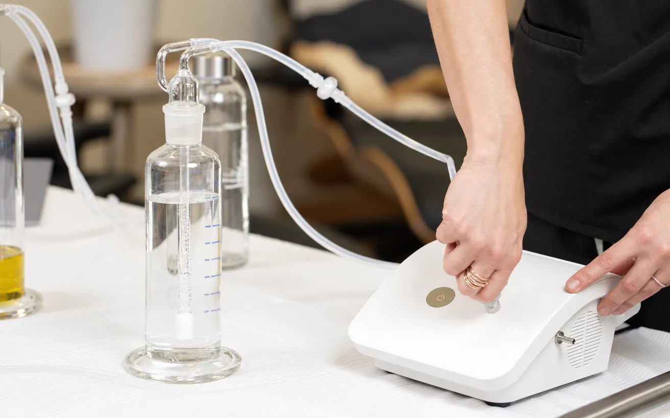Hands switching on a home ozone generator connected by clear tubing to glass bubbler bottles of water and oil
