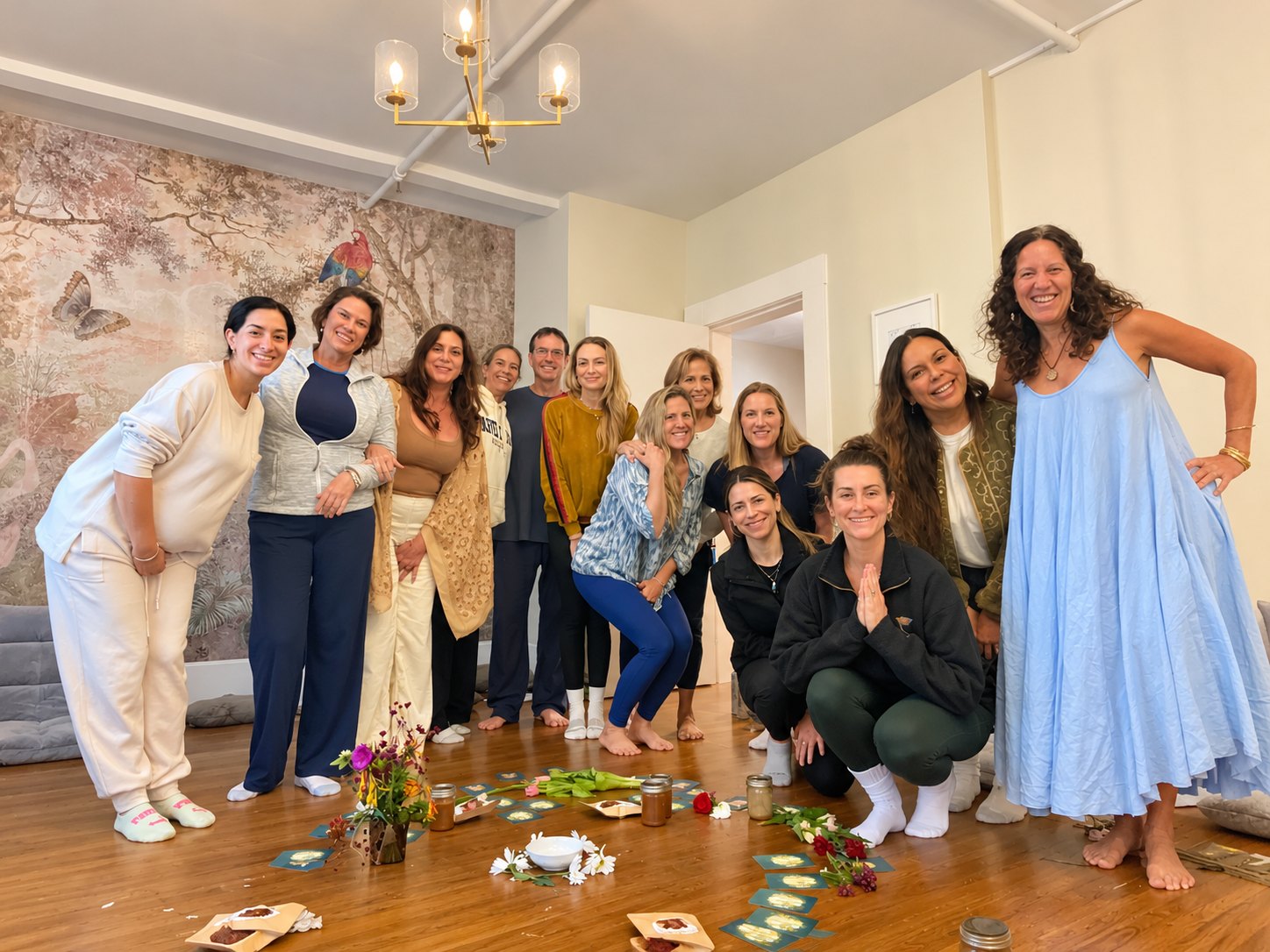 A group gathered and smiling in the Monarch Soul studio after a Chrysalis Circle, with flowers, candles and cards laid out on the floor