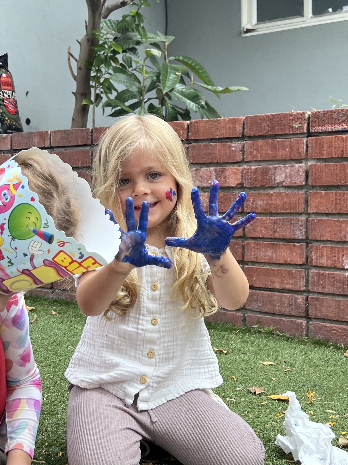 A young girl holding up hands covered in blue paint at a Monarch Kids art session