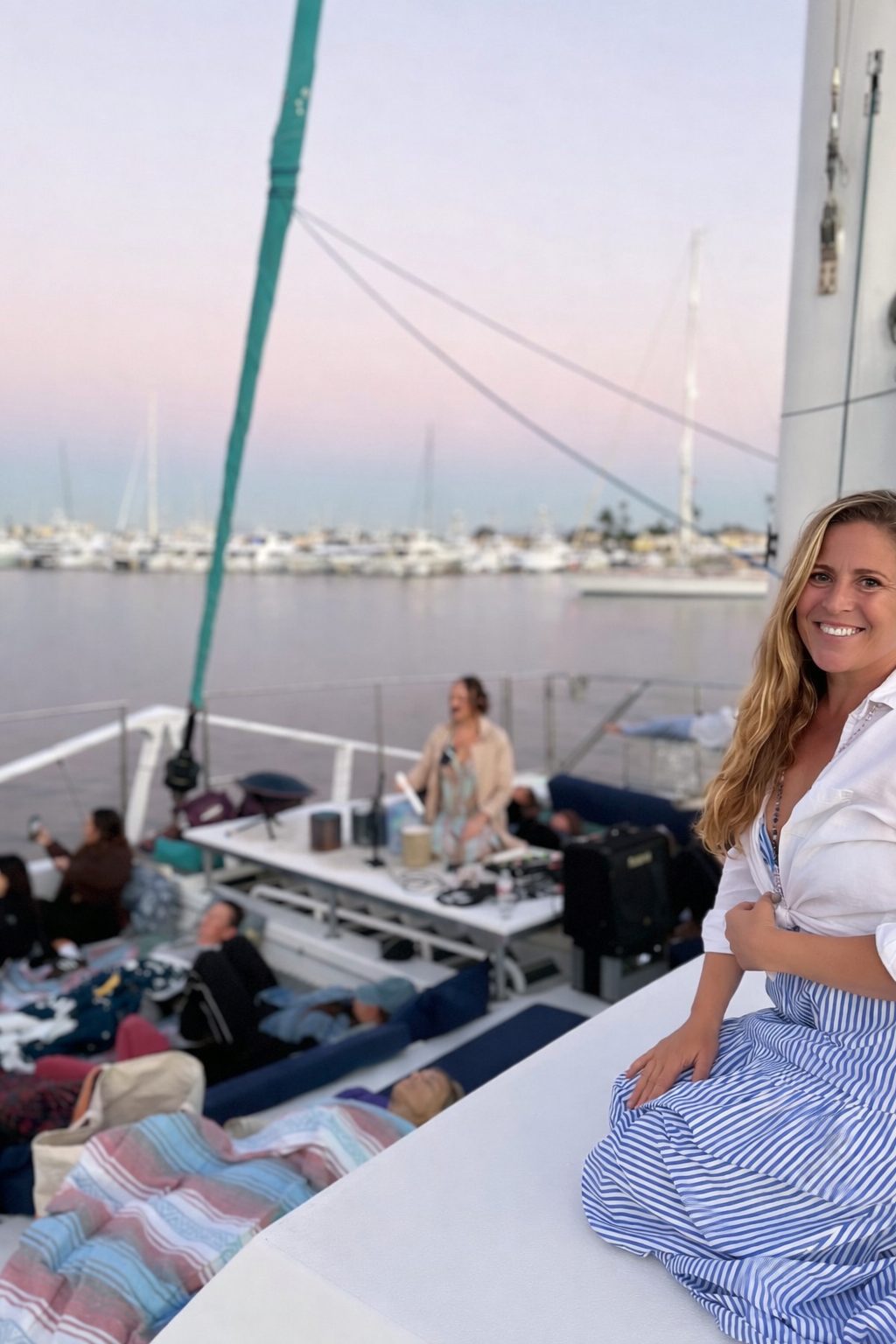 Stephanie smiling on a sailboat at dusk with guests gathered for a private Monarch Soul experience