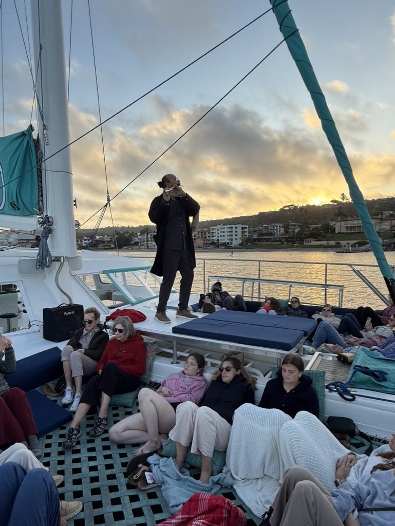 A group relaxing on the deck of a catamaran at sunset during a Monarch Soul sound experience