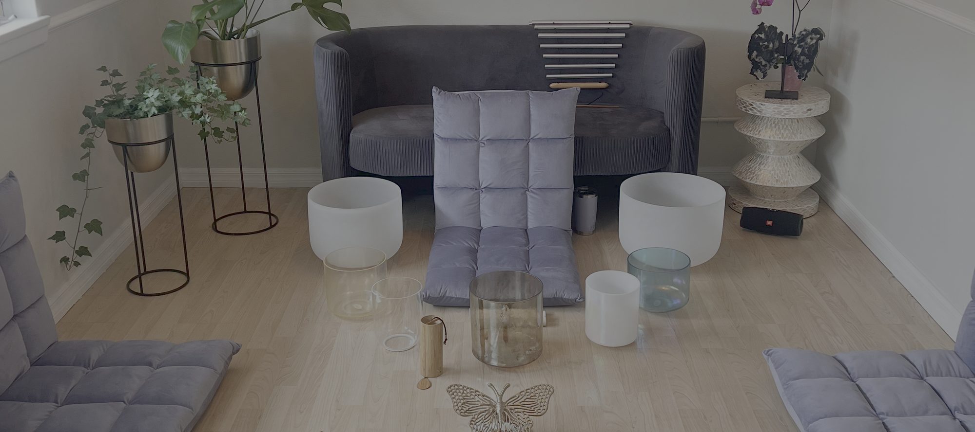 The Monarch Soul studio set for a sound session, with crystal singing bowls, floor cushions and a brass butterfly in front of a velvet sofa