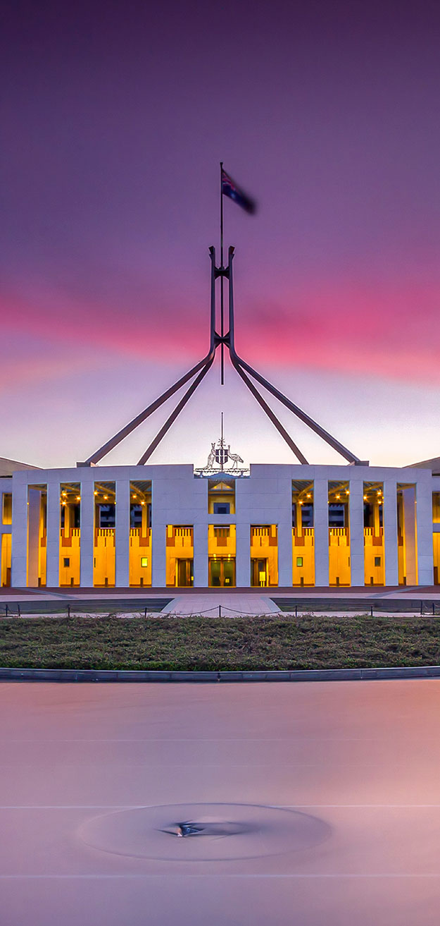 Australian Federal Parliament House at sunset with pink clouds behind.