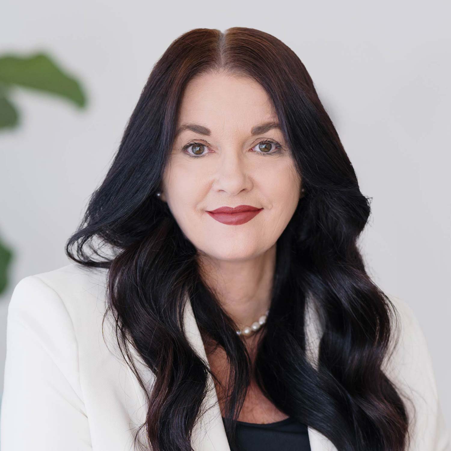 Photo of Janine Morice with long dark wavy hair, and white jacket with pearls.