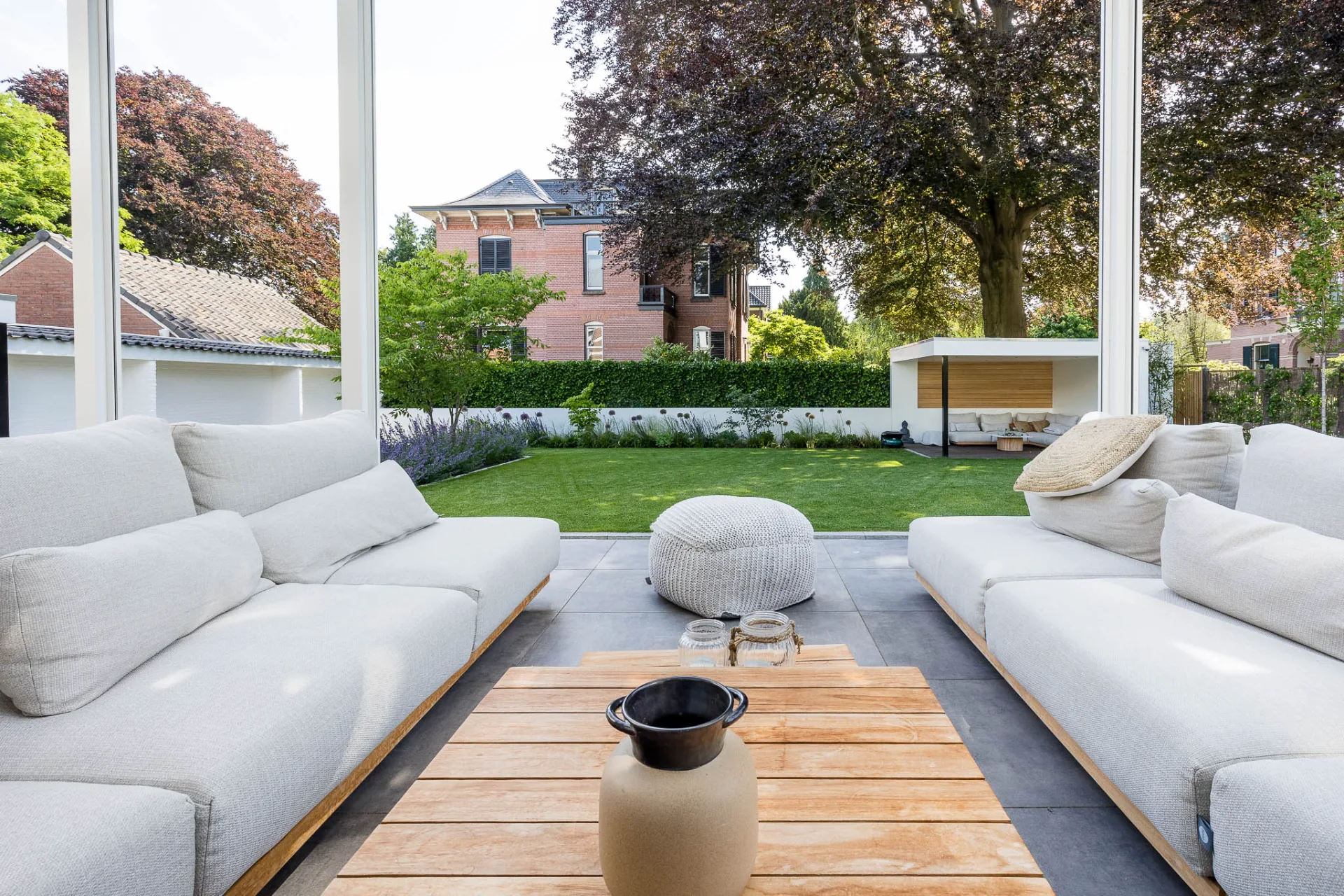 Overkapping met loungebank en zicht op een onderhoudsvriendelijke tuin met gazon, borders en tuinhuis door Mecklenfeld tuinen