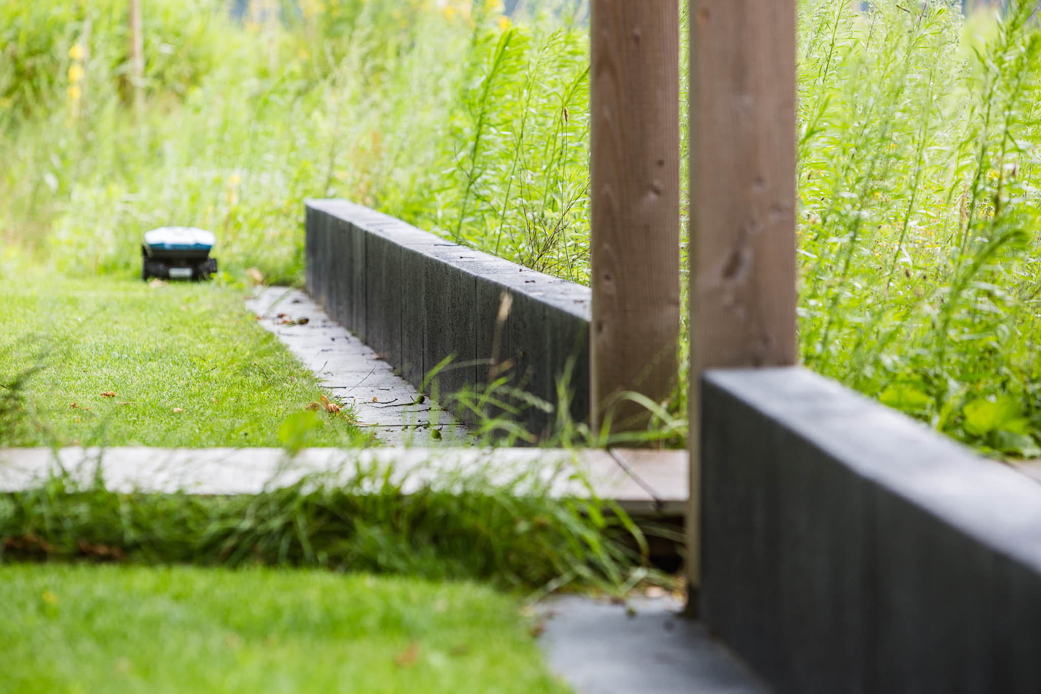 Robotmaaier op het gazon langs betonnen opstaanden in een onderhoudsvriendelijke tuin in Stegeren