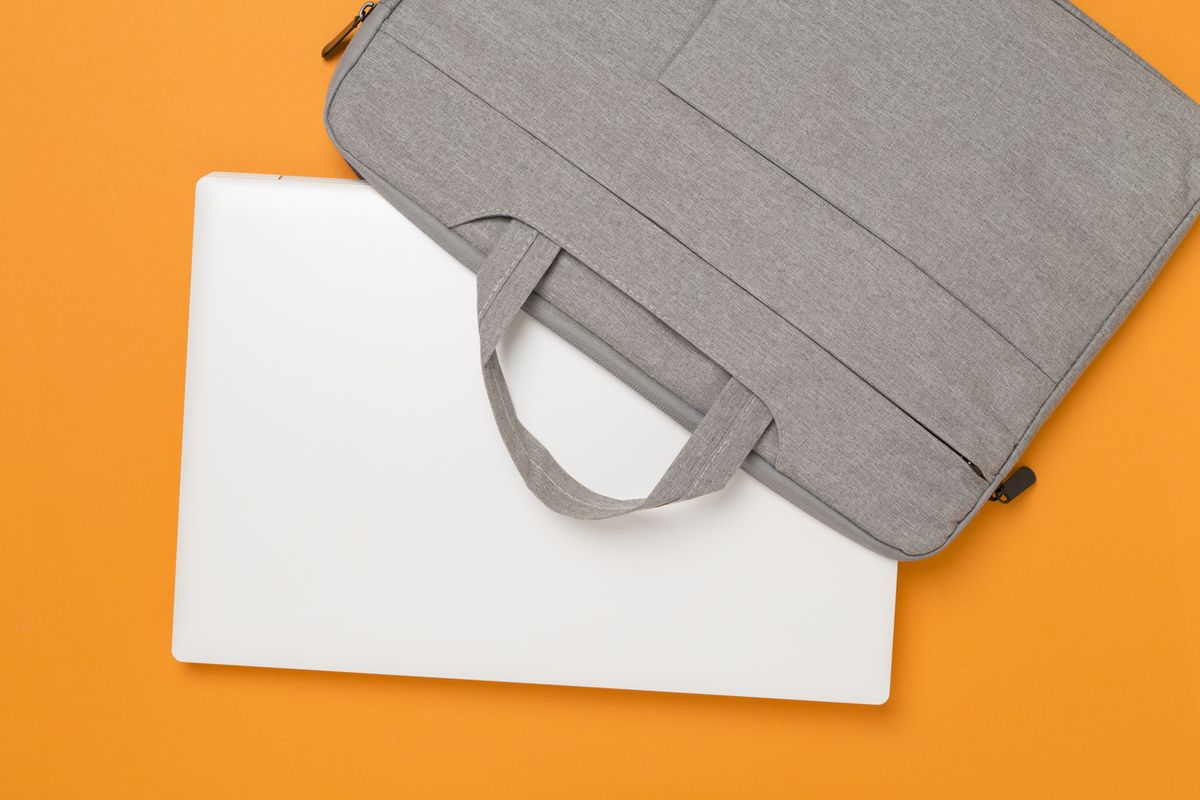 Closed white laptop partly covered by a grey fabric laptop bag, on an orange surface