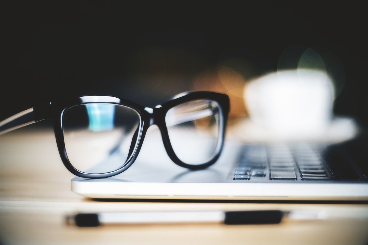 Black-framed glasses resting on an open laptop, with a coffee cup out of focus behind