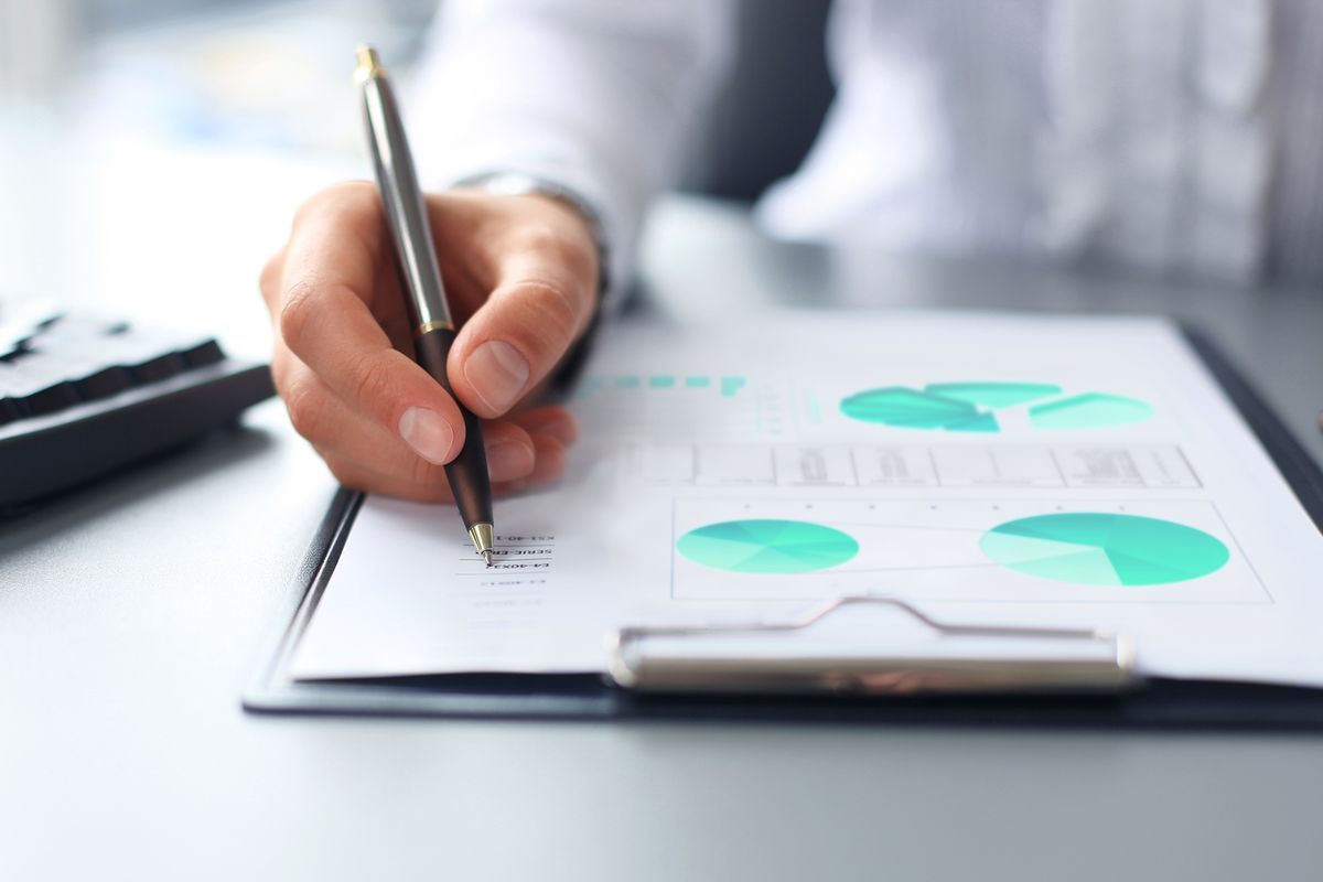 A hand holding a pen over a clipboard of printed pie charts