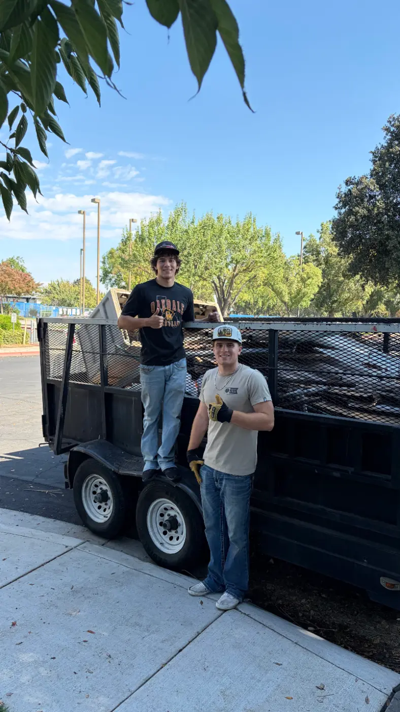 Jake and a crew member giving a thumbs up beside a fully loaded junk trailer
