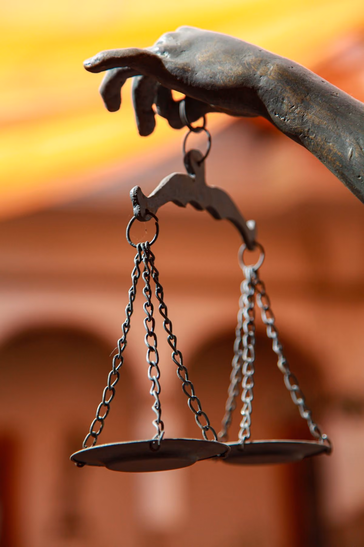 Bronze scales of justice held up against a warm architectural background