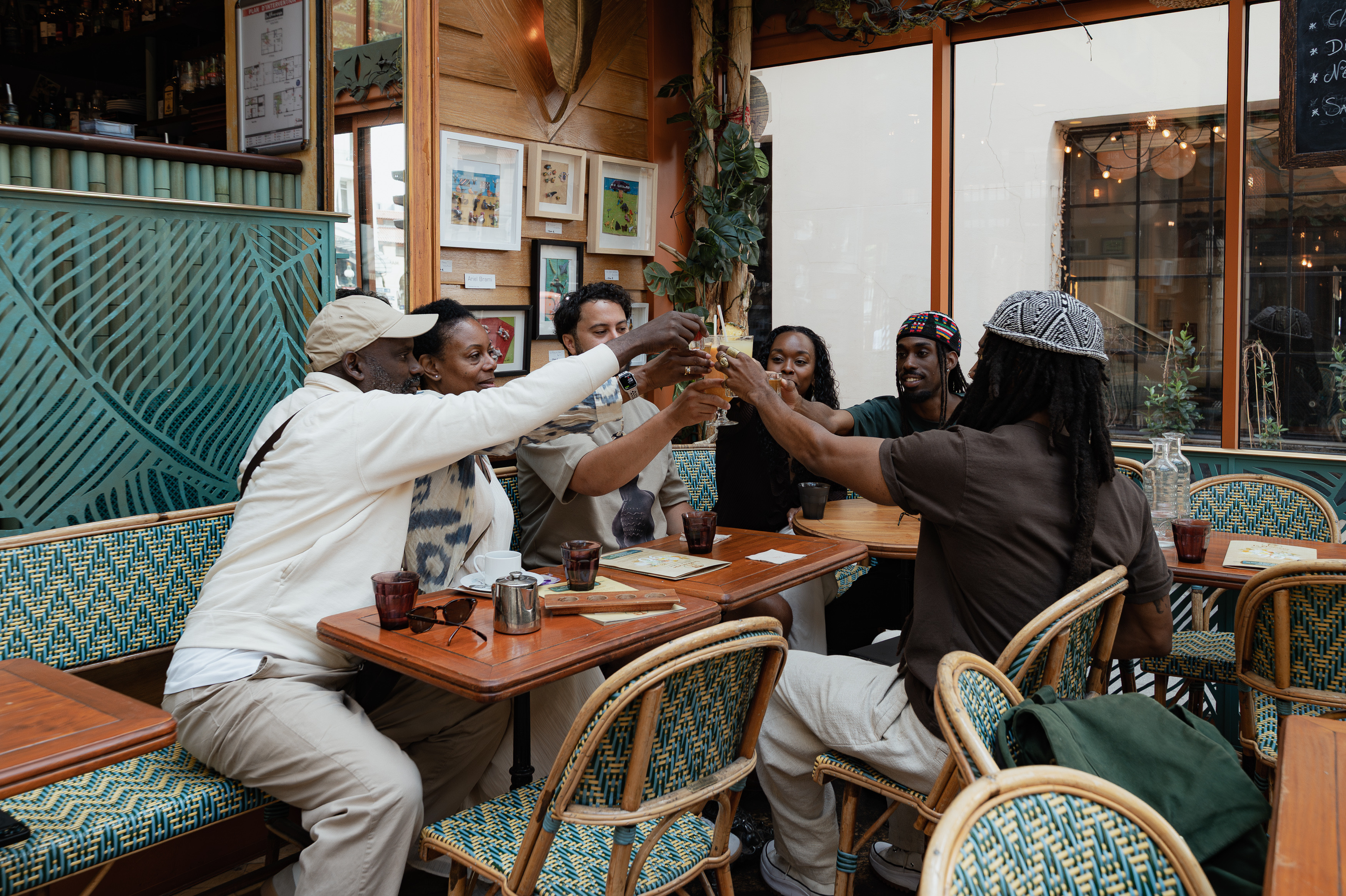 Group raising their glasses together at a restaurant during the AfroNomadik Paris photoshoot