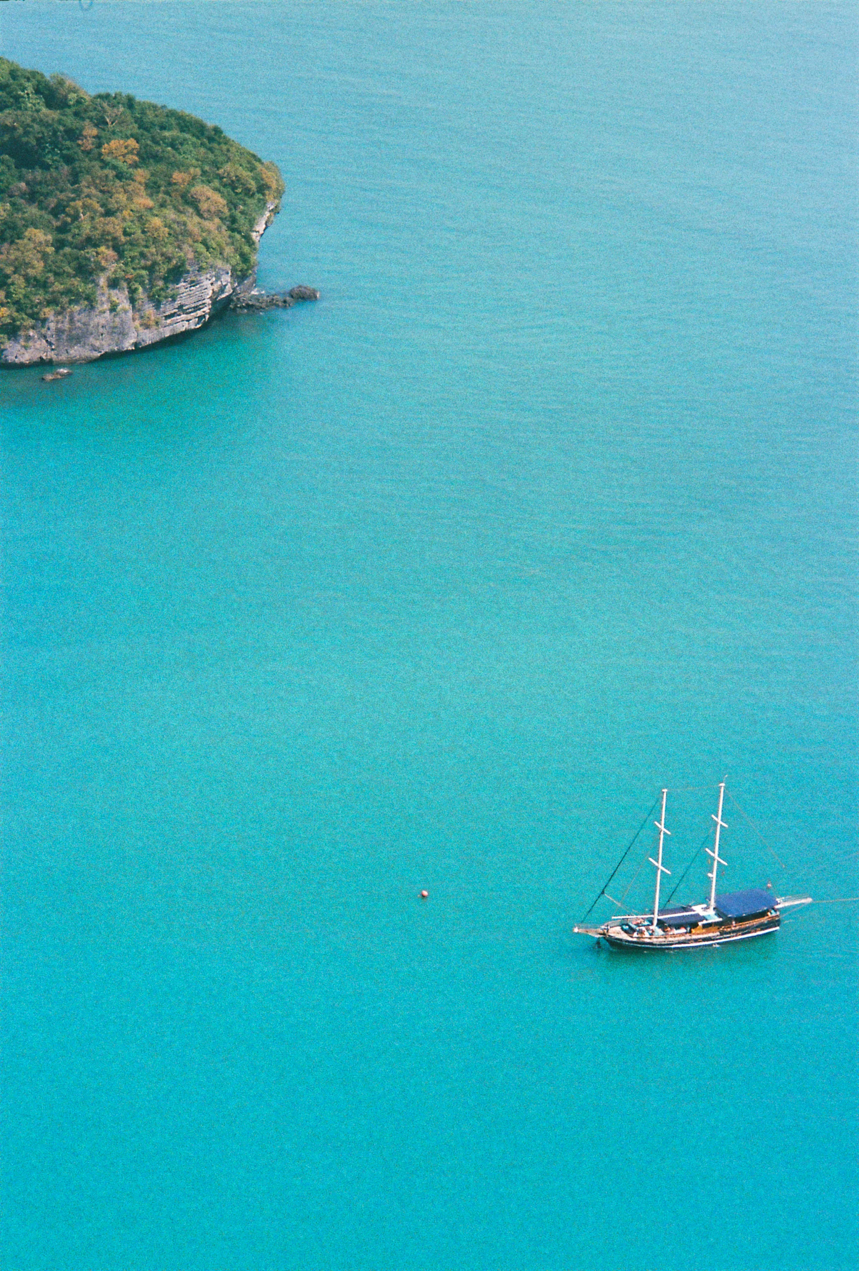 Mer turquoise, un voilier au pied d'une île boisée