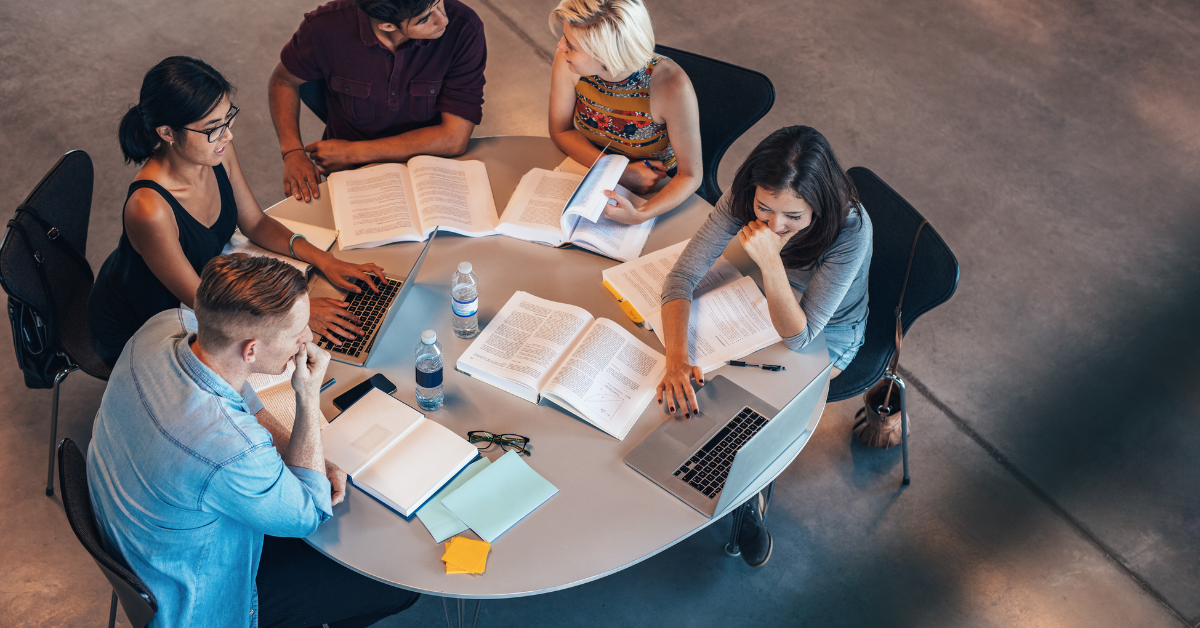 Students working around a table with laptops and books