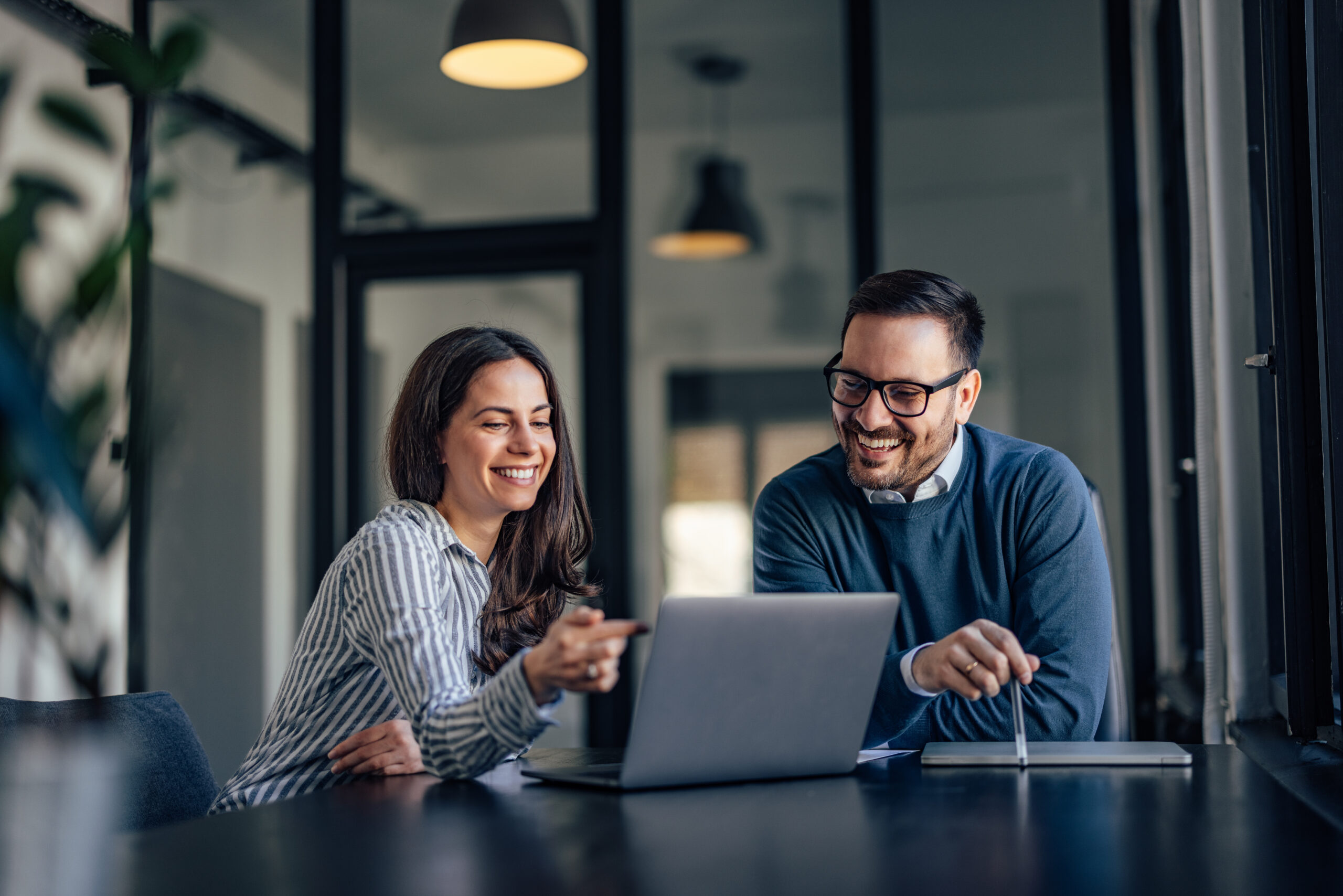 Two colleagues smiling while working at a laptop