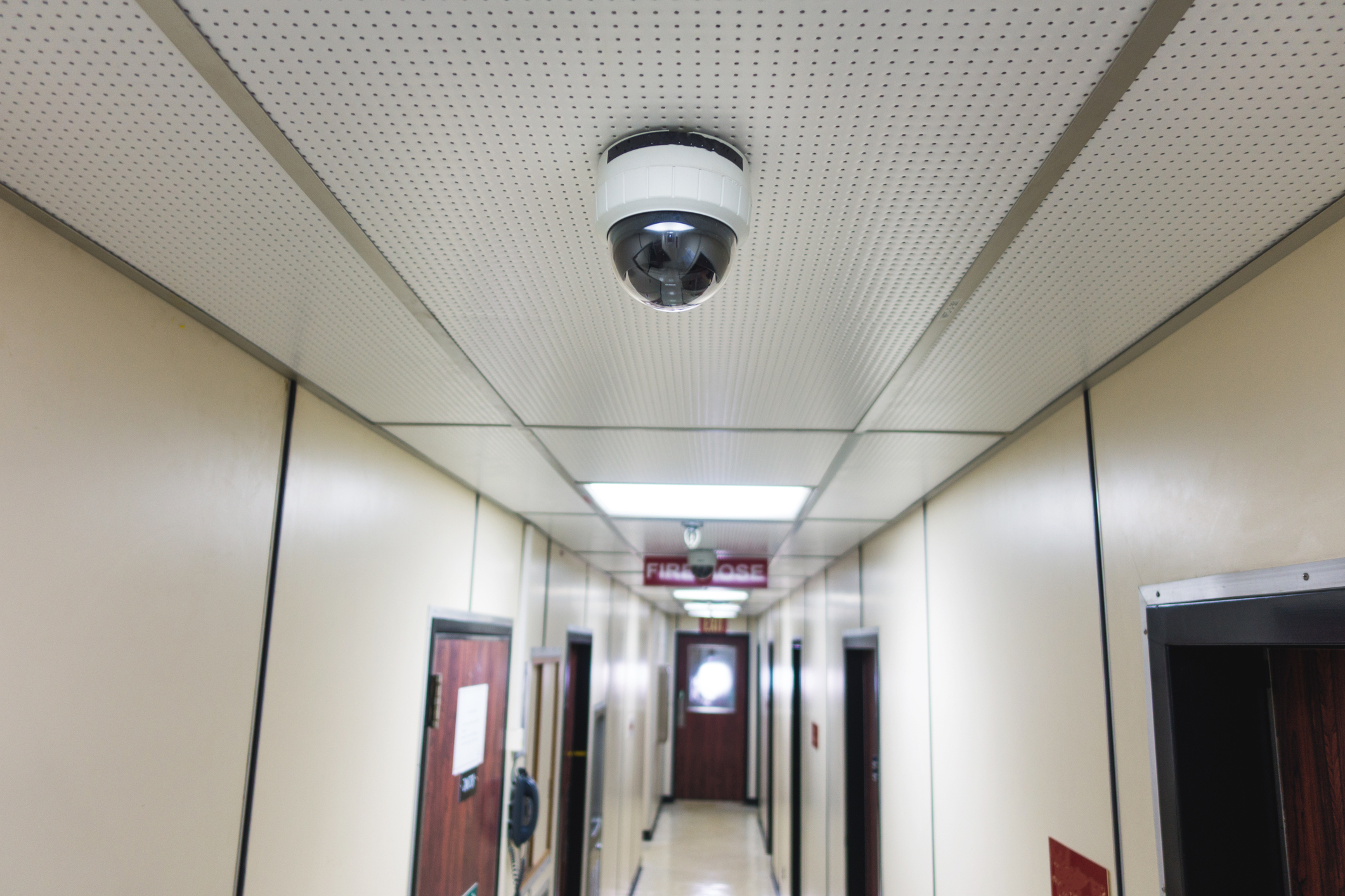 A dome security camera on the ceiling of a school hallway