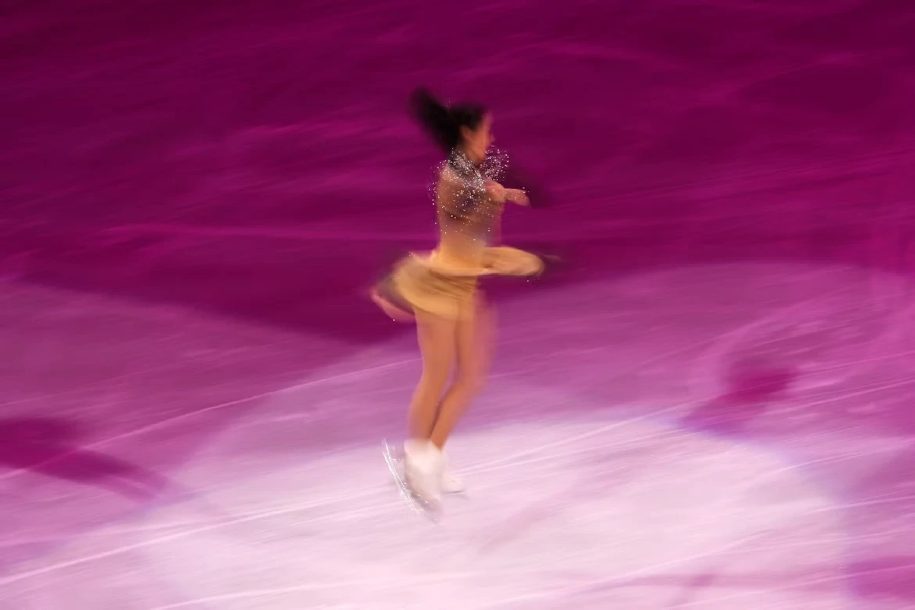 A figure skater mid-spin under pink light