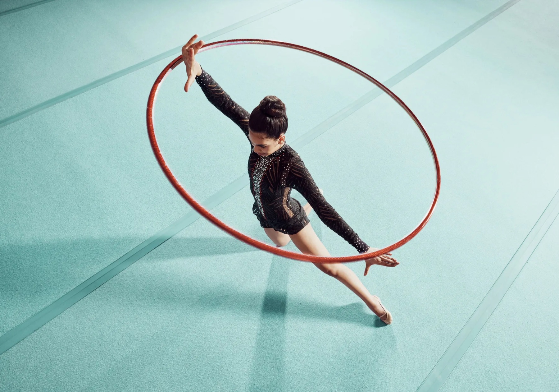 A rhythmic gymnast performing with a red hoop, seen from above